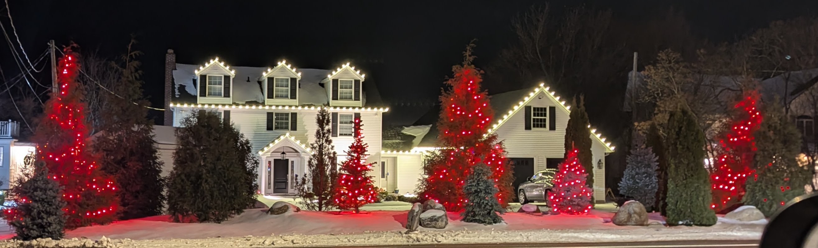 Red trees and white roofline lights on a snow-covered property